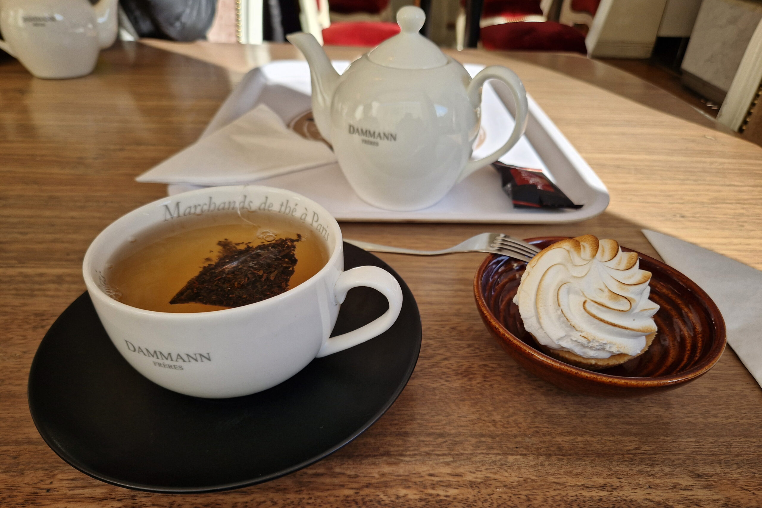 A tea pot, a cup of tea, and a pastry on a plate, standing on a table, at Karla Café in Stockholm Sweden.