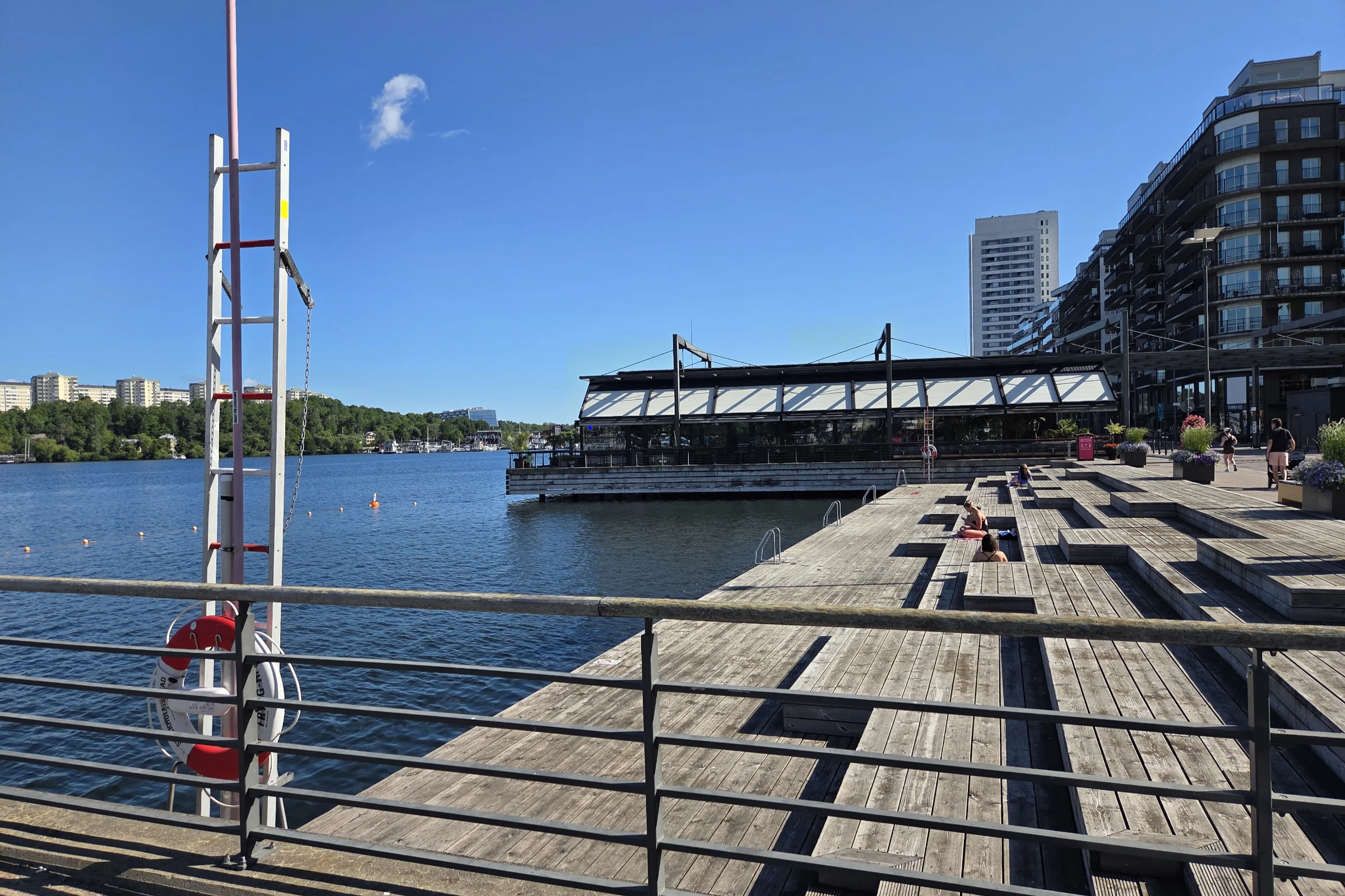 Kristinebergsbadet in Kungholmen, in Stockholm on a sunny summer morning, with a few sunbathers sitting on the wooden deck.