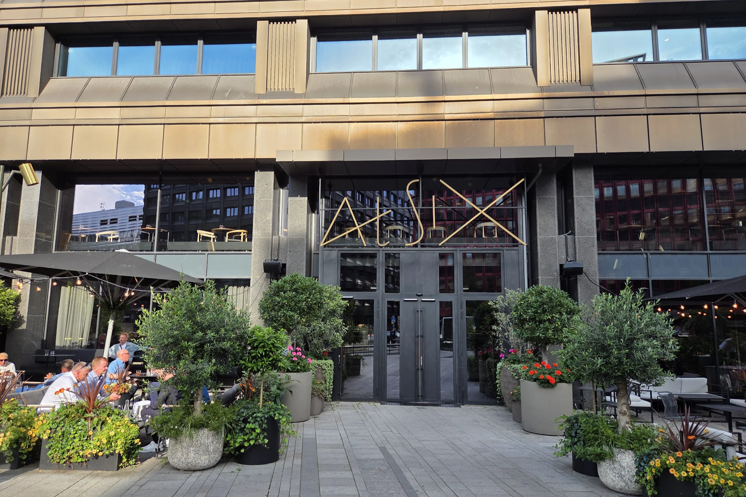 The entrance to the At Six hotel in Stockholm, with plants and flowers surrounding the entrance with its glass and metal facade.
