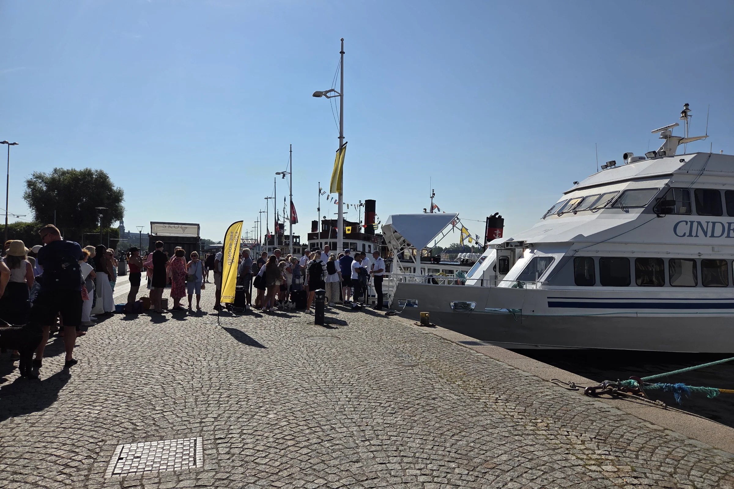 The line to board the Cinderellabåtarna boat Cinderella II going to Sandhamn. People standing at Strandvägen, waiting to board the ship.