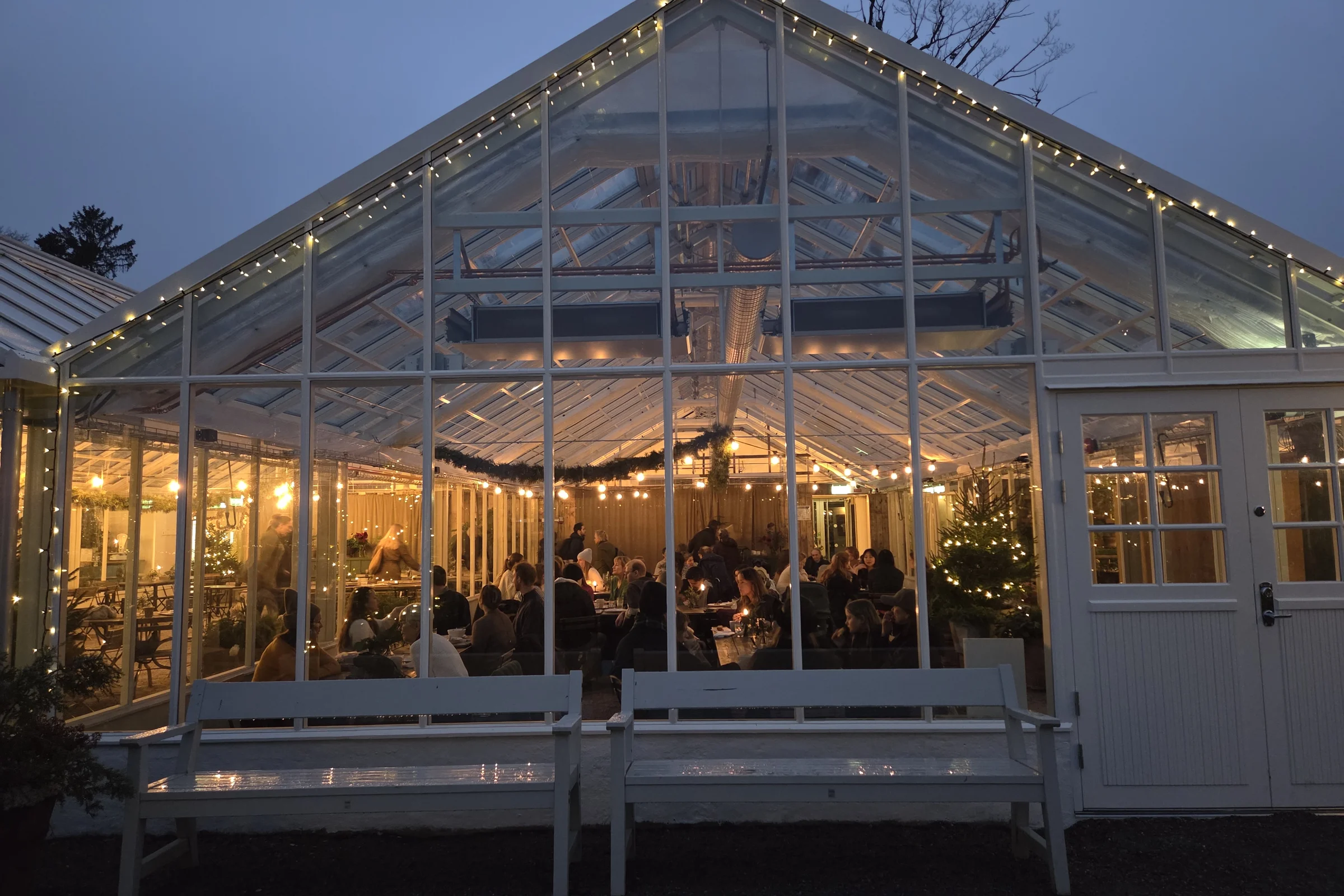 Rosendals Trädgård indoor café during a winter night, illumanted with people sitting indoors having a Swedish fika.